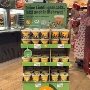 Farbige Mehrwegbecher stehen in einer modernen Küche auf einer Arbeitsplatte, umgeben von Pflanzen und umweltfreundlichen Utensilien.