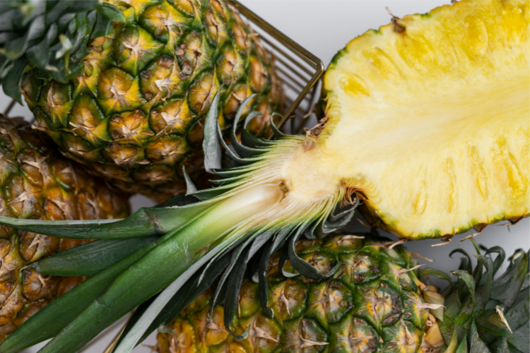 Ananas – halbiert – liegt in einem Korb mit ganzen Ananasfrüchten.